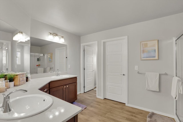 bathroom with double vanity, a stall shower, a sink, and wood finished floors