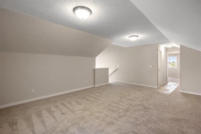 additional living space with carpet flooring, vaulted ceiling, a textured ceiling, and baseboards