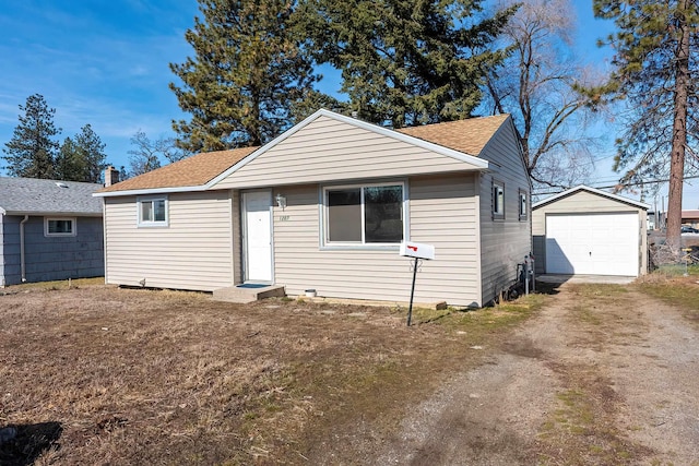 bungalow with driveway, a shingled roof, a garage, and an outdoor structure