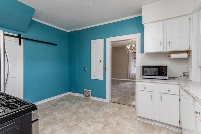 603 N Main St, Colville, WA 99114 - kitchen with stainless steel microwave, a chandelier, white cabinets, light countertops, and ornamental molding