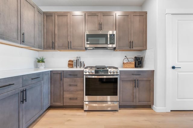 kitchen featuring light wood-style floors, decorative backsplash, stainless steel appliances, and light countertops