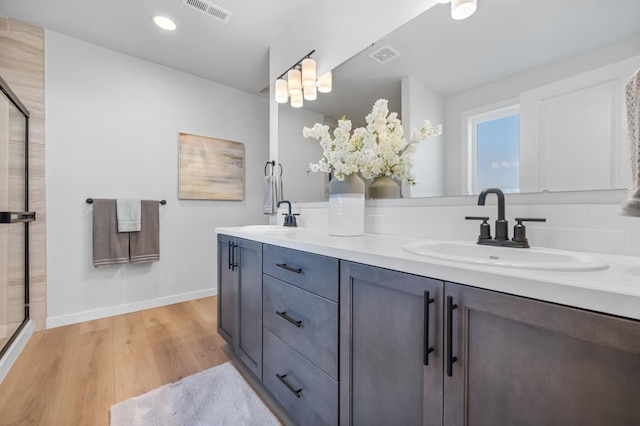 full bathroom with wood finished floors, a sink, visible vents, and a shower with door