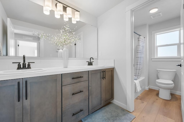 full bath with double vanity, visible vents, a sink, and wood finished floors