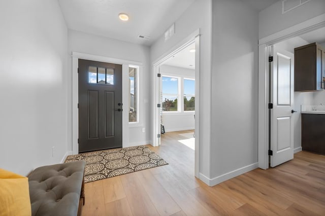 foyer featuring light wood finished floors, baseboards, and visible vents