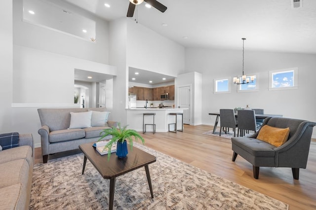 living room featuring high vaulted ceiling, light wood-style flooring, recessed lighting, ceiling fan with notable chandelier, and baseboards