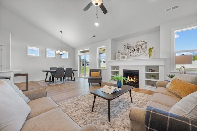 living area with ceiling fan with notable chandelier, wood finished floors, visible vents, baseboards, and a glass covered fireplace