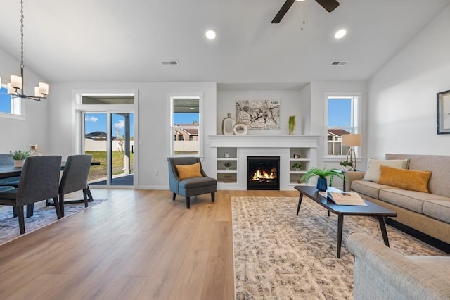 living area with recessed lighting, visible vents, vaulted ceiling, a lit fireplace, and light wood finished floors