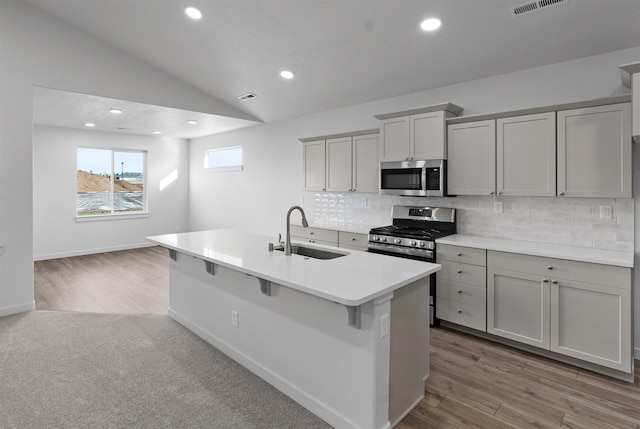 kitchen featuring tasteful backsplash, lofted ceiling, gray cabinets, appliances with stainless steel finishes, and a sink