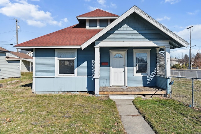 bungalow-style house with covered porch, roof with shingles, a front yard, and fence