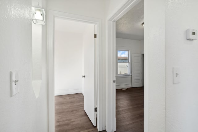 hall with a textured ceiling, baseboards, wood finished floors, and a textured wall