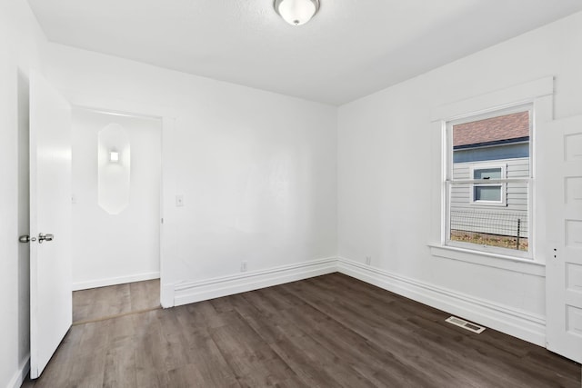 empty room with dark wood finished floors, visible vents, and baseboards