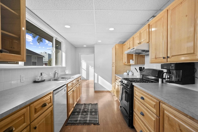 kitchen with dishwasher, black gas range oven, dark wood-style flooring, under cabinet range hood, and a sink