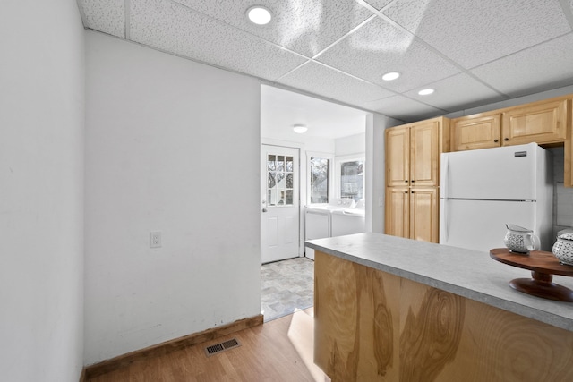 kitchen with light wood finished floors, visible vents, freestanding refrigerator, washing machine and dryer, and light brown cabinets