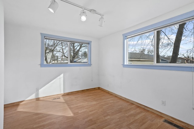 unfurnished room with rail lighting, baseboards, visible vents, and wood finished floors