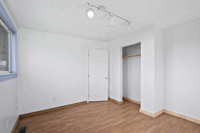 unfurnished bedroom with baseboards, visible vents, wood finished floors, rail lighting, and a closet