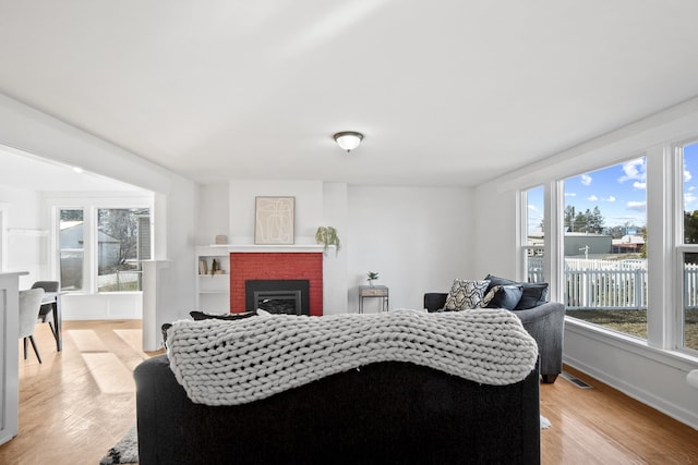 living room with light wood finished floors, baseboards, a brick fireplace, and visible vents