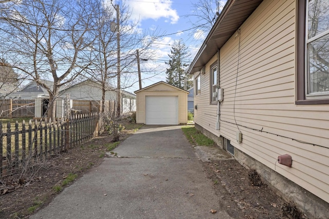 view of property exterior with driveway, a detached garage, fence, and an outdoor structure