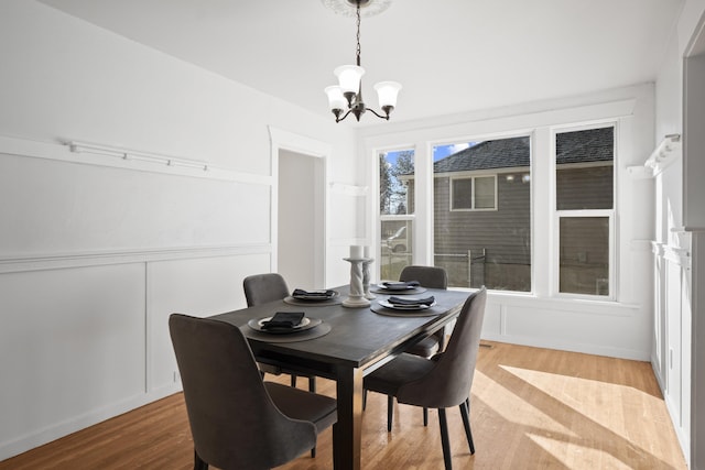 dining room featuring light wood-style floors, a decorative wall, and an inviting chandelier