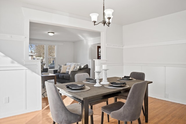 dining space with a wainscoted wall, a decorative wall, light wood-type flooring, and an inviting chandelier