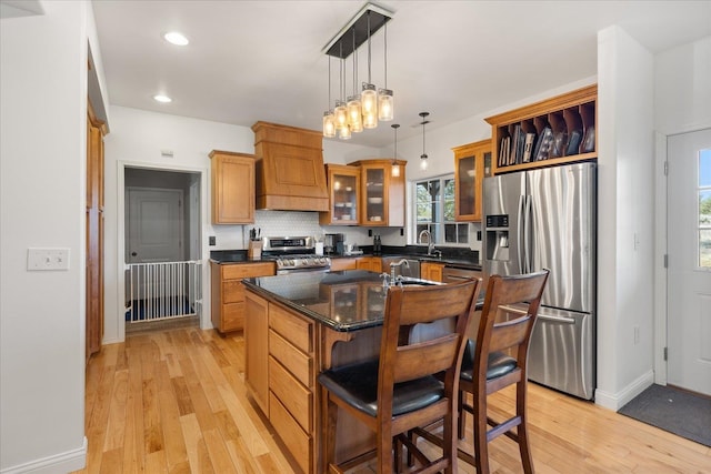 kitchen with a breakfast bar area, light wood-style flooring, premium range hood, appliances with stainless steel finishes, and backsplash