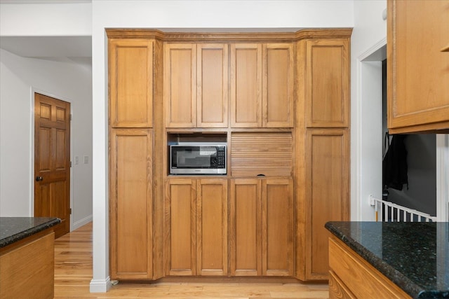 kitchen featuring light wood finished floors, stainless steel microwave, and dark stone countertops