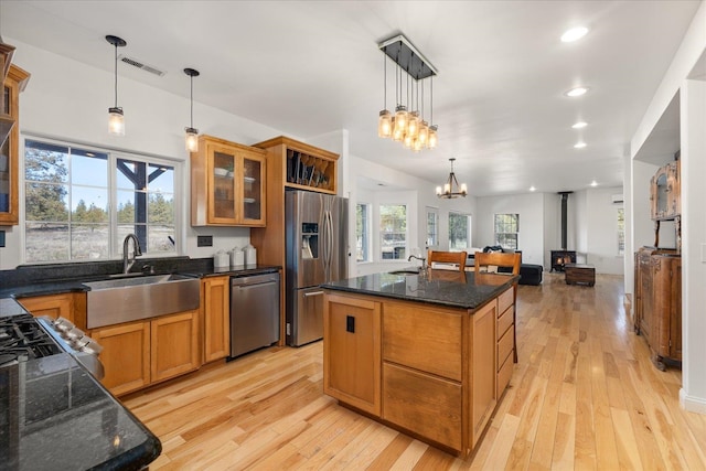 kitchen featuring visible vents, brown cabinets, a wood stove, stainless steel appliances, and a sink