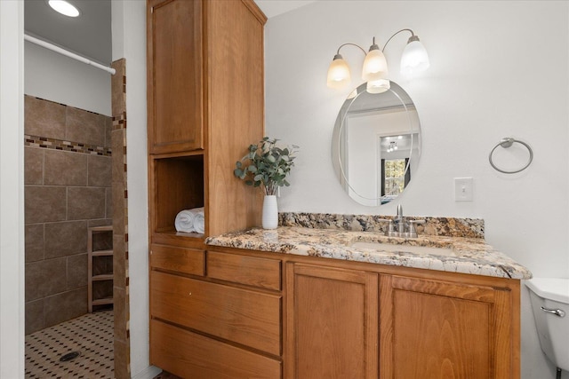 bathroom with a tile shower, vanity, and toilet