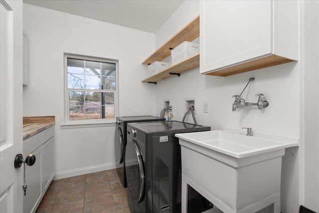 clothes washing area with cabinet space, baseboards, washer and clothes dryer, stone finish flooring, and a sink