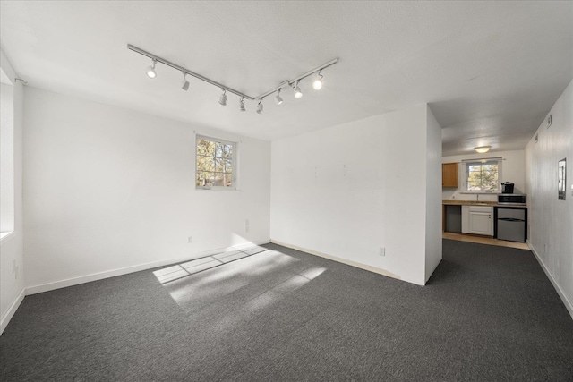 unfurnished room with dark colored carpet, a wealth of natural light, and baseboards