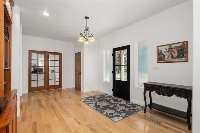 entryway with light wood-type flooring, french doors, a notable chandelier, and baseboards