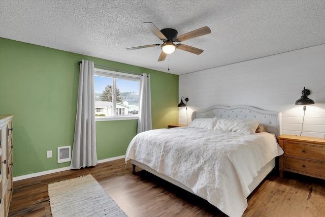 bedroom with baseboards, a textured ceiling, visible vents, and wood finished floors