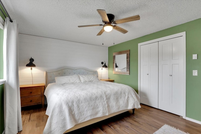 bedroom featuring a closet, a ceiling fan, a textured ceiling, wood finished floors, and baseboards