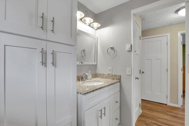 bathroom featuring baseboards, vanity, a textured ceiling, and wood finished floors