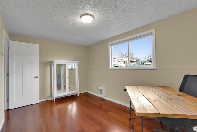 unfurnished office featuring a textured ceiling, baseboards, and wood finished floors