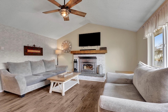 living area with a textured ceiling, a fireplace, wood finished floors, a ceiling fan, and vaulted ceiling