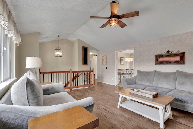 living area featuring lofted ceiling, a textured ceiling, wood finished floors, a ceiling fan, and baseboards