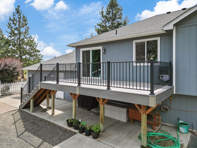 rear view of property with a deck, a patio, a garage, a shingled roof, and stairs