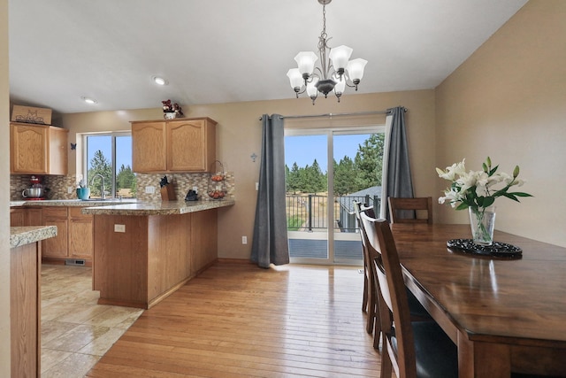 kitchen featuring decorative backsplash, light wood-style flooring, a peninsula, a chandelier, and a sink