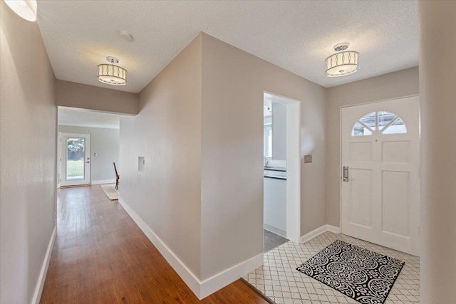 entrance foyer with baseboards, a textured ceiling, and light wood finished floors