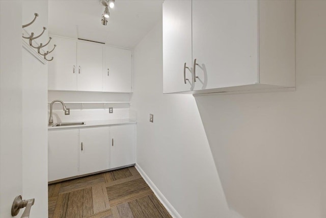 kitchen featuring baseboards, light countertops, a sink, and white cabinets