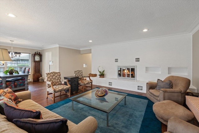 living area with a notable chandelier, ornamental molding, a large fireplace, a textured ceiling, and wood finished floors