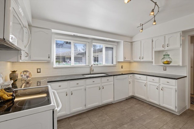 kitchen with white appliances, white cabinets, dark countertops, vaulted ceiling, and a sink