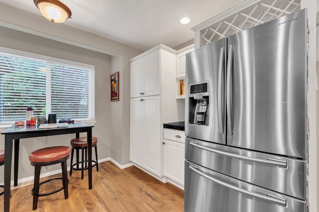 kitchen with light wood finished floors, dark countertops, white cabinets, stainless steel fridge, and baseboards