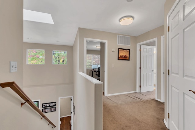 hall with a skylight, baseboards, visible vents, an upstairs landing, and carpet floors