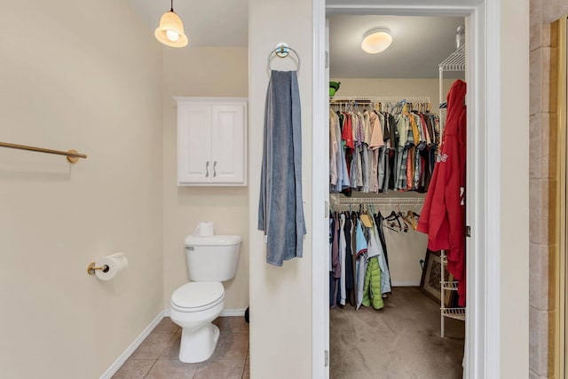bathroom with tile patterned flooring, a walk in closet, toilet, and baseboards