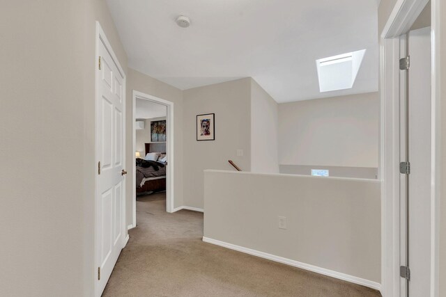 hallway with carpet, a skylight, an upstairs landing, and baseboards