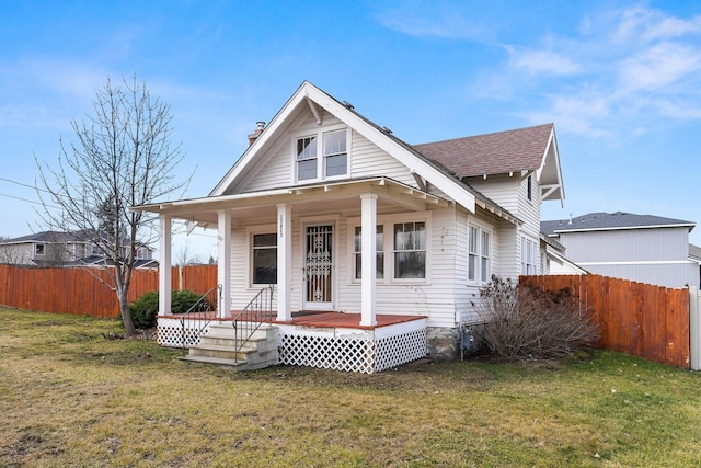 bungalow with a porch, fence, a shingled roof, and a front lawn