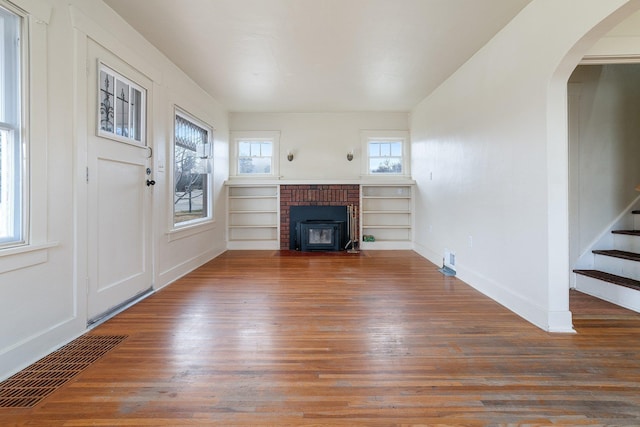 unfurnished living room featuring arched walkways, visible vents, stairway, and wood finished floors