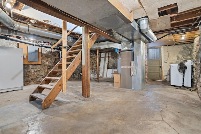 unfinished below grade area featuring heating unit, washing machine and dryer, freestanding refrigerator, and electric panel