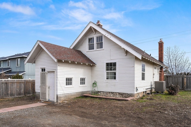 back of house with a shingled roof, a chimney, fence, and cooling unit